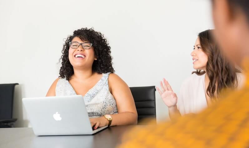 Two women laughing around a laptop