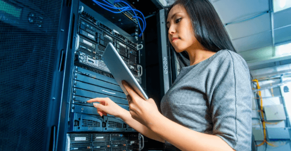 Photo of a woman in a server room looking at a tablet computer