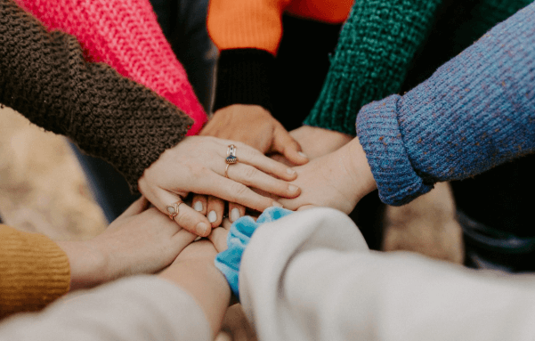 Photo of people putting their hands together in the middle of a circle.